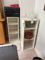 Shows two small white pressboard shelving units side by side; one is empty and one holds decorative glass bowls (not included). Dimensions approximately 12x12x32 inches.