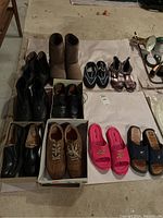 Photo showing nine pairs of assorted footwear including boots, dress shoes, casual shoes, slides, and sandals arranged on the floor.
