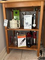 Wolfgang Puck Food Prep Center knife, Cuisinart blender set, citrus juicer, electric immersion blender, and various utensils displayed on wooden shelf.