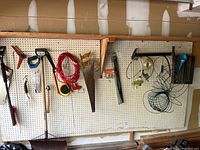 Photo showing hand saws, shovel, extension cord, and other tools hanging on pegboard wall
