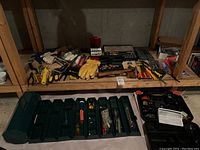 Wide view of multiple tools on wooden shelves and green toolboxes on floor showing variety of tools and paint supplies