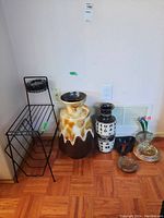 Photo showing metal stand with ashtray, large brown and cream ceramic vase, white Germany jug with Asian characters, small glass vase with faux floral, decorative ashtrays on floor