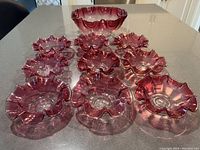 Set of 1 large pink glass bowl and 9 smaller matching pink glass dishes with ruffled edges, displayed on countertop.