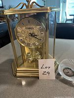 Brass clock with glass panels and ornate dial seen from front, clear view of rotating pendulum balls