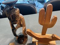 Four wooden items on a surface: carved wooden figure and cactus-shaped serviette holder