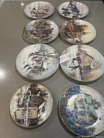 Top view of 8 Keirstead plates arranged on countertop showing detailed winter village and rural scenes with gold trim.