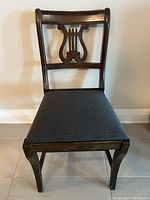 Front-side view of the antique chair showing the dark wood frame, lyre design backrest, and upholstered seat cushion.
