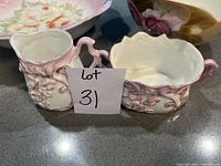 Close-up of the antique cream and sugar set with pink floral relief detailing, showing the ornate handles and white glaze.