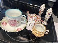 Photo showing the full set: cup and saucer with pink rose floral pattern, teapot with colorful floral pattern, pair of matching floral salt and pepper shakers, and ornate yellow sugar bowl.