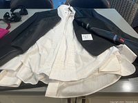 Black tuxedo jacket and two white dress shirts spread out on a table showing detail and condition.