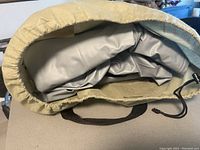 Close-up of the air mattress folded inside a beige-green carrying bag, showing gray vinyl material and drawstring opening.