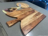 Two wooden charcuterie boards and one round acrylic board on countertop.