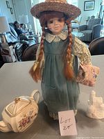 Anne of Green Gables doll standing on a table beside a small ceramic floral teapot and a white Disney castle figurine, showing the main lot items.