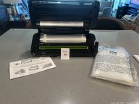 FoodSaver vacuum sealer open, showing roll of seal bags inside and instruction manual beside it.