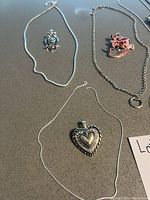 All necklace chains and clip-on charms laid out flat on a gray surface, showing variety of chain styles and several charms.