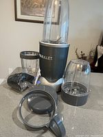 Nutribullet base with blending cup attached, two extra cups, multiple gray lids, and power cord on countertop.