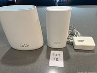 Photo of Orbi WiFi router, satellite extender, and power adapter on gray surface, with Lot 12 note visible.