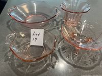 Top view of set showing three pink glass bowls in different shapes and one pink glass vase with flared, scalloped rim, all displayed on a countertop with good lighting.