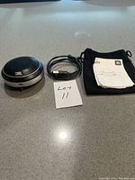 JBL speaker, USB charging cable, user manual, and black fabric pouch arranged on countertop.