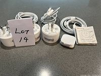 Three white smart plugs with attached cables and two user manuals on a gray surface. Prongs visible on plugs.