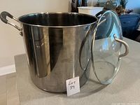 Large stainless steel soup pot with metal handles and clear glass lid shown off to the side.