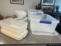 Two large translucent storage containers with blue handles and eight smaller containers with lids stacked, placed on kitchen countertop.