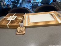 Photo showing a large wooden tray with white base and handles, three smaller trays nested inside it, a large square wicker tray, a set of four cork coasters with decorative print, and the white cracker and dip dish tied with a ribbon.