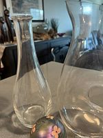 Two clear glass wine decanters and one floral painted glass ball placed on a surface with a black cabinet background.