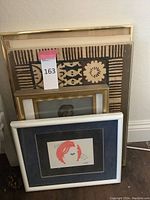 Four framed artworks stacked against wall, showing various frame styles and matting conditions including gold frame and white frame