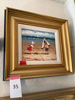 Full view of the framed oil painting showing children playing on the beach with a boat and ocean background