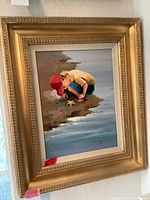 Frontal view of the gold framed painting depicting a young child examining a starfish on the shore.