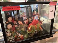 Glass display case with approximately 10 Asian dolls dressed in traditional costumes inside, clear view of multiple dolls robed in different colorful fabrics.