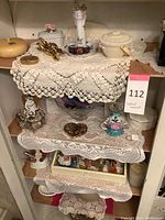 Overall view of shelves with decorated ceramic and glass items on crocheted lace doilies.