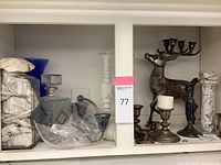 Shelf with various candlesticks including silver and silver plated, glass decanter, and clear glass vase.