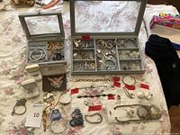 Photo showing multiple jewelry cases containing bracelets, rings, necklaces, brooches, and earrings, with red tags marking 925 silver items and Mexican silver noted.