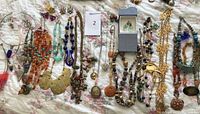 Overview of the entire jewelry lot spread out on a floral bedspread showing multiple beaded necklaces, metal pendant necklaces, and earrings.