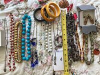 All costume jewelry items laid out on a floral sheet including beaded necklaces, chunky gold chain bracelet, bangles, earrings in box, and various other necklaces and bracelets.