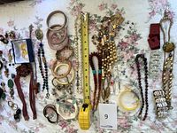 Photo showing the full assortment of costume jewelry laid on floral fabric, including bracelets, necklaces, earrings, and measuring tape for scale.