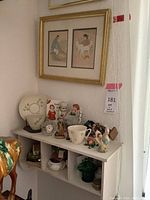 White wall-mounted shelf with Beleek porcelain items, Waterford crystal desk clock, small decorative figurines, beneath a framed double Native American prints artwork.