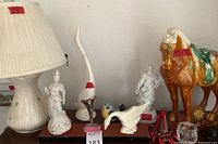 Photo showing Beleek ceramic lamp, white ceramic statues including Asian style and bird figures, and large ceramic horse with missing tail.