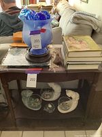 Blue glass bowl on stand with blue and green watering globes inside, stacked books on table, ceramic cats holding bowls on lower shelf