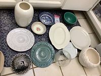 Various bowls, plates, and two white ceramic vases displayed on the floor