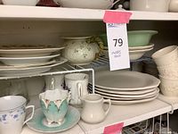 Overview of upper shelf with stacked plates, cups, bowls, and tea canister.