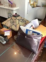 Arts and crafts style lamp with stained glass shade, next to a dark brown folder full of mail and papers on a glass tabletop