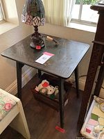 Photo of small black wooden table with acorn motif, showing square top and four legs with wooden box of stuffed toys underneath.