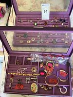 First purple case open showing rings in slot rows and assorted bracelets/earrings below