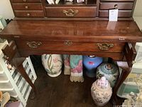 View of vintage wooden desk with a polished finish, showing the front with closed side drawers and central big drawer beneath desk surface.