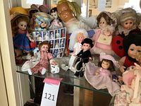 Photo shows a collection of vintage dolls displayed in a cabinet, including a doll stamp set, dolls dressed in period clothing, and various doll types.