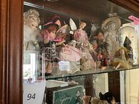 Wide view of vintage doll collection inside a cabinet showing multiple dolls with a focus on the whole lot