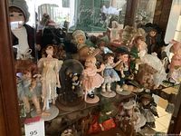 Overview of vintage dolls inside a glass cabinet showing a variety of dolls in period clothing.